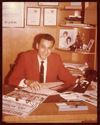 Syd Freedman sitting behind a cluttered desk while holding a poster