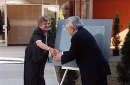 SJC beneficiaries shaking hand in front of St. John's College UBC plaque